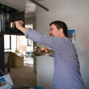 Man with down syndrome living independently putting cups away in home